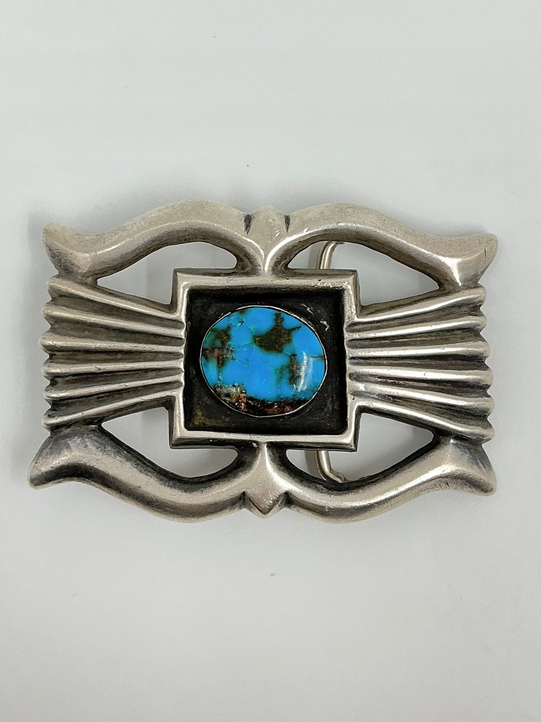 Silver belt buckle with a central turquoise stone on a white background