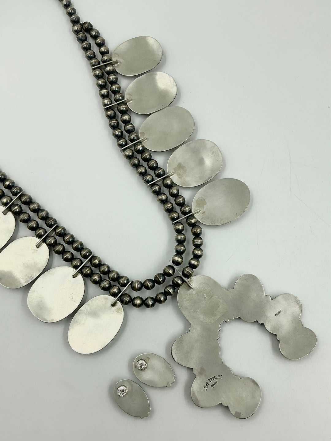 Back of set with necklace, earrings, and Naja pendant showing stamped silver on a light gray background. 