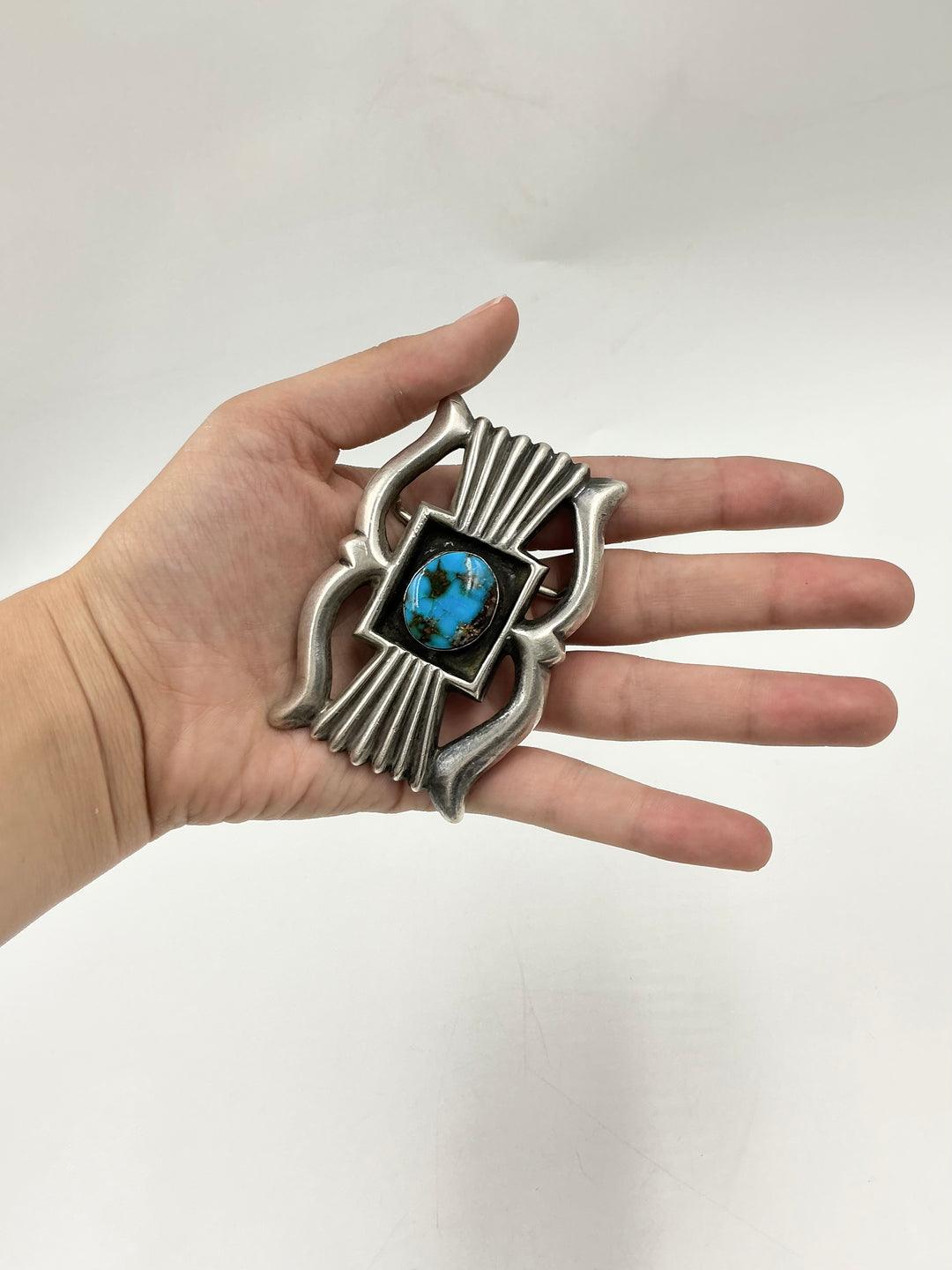 Hand holding a decorative silver object with a blue gemstone on a white background