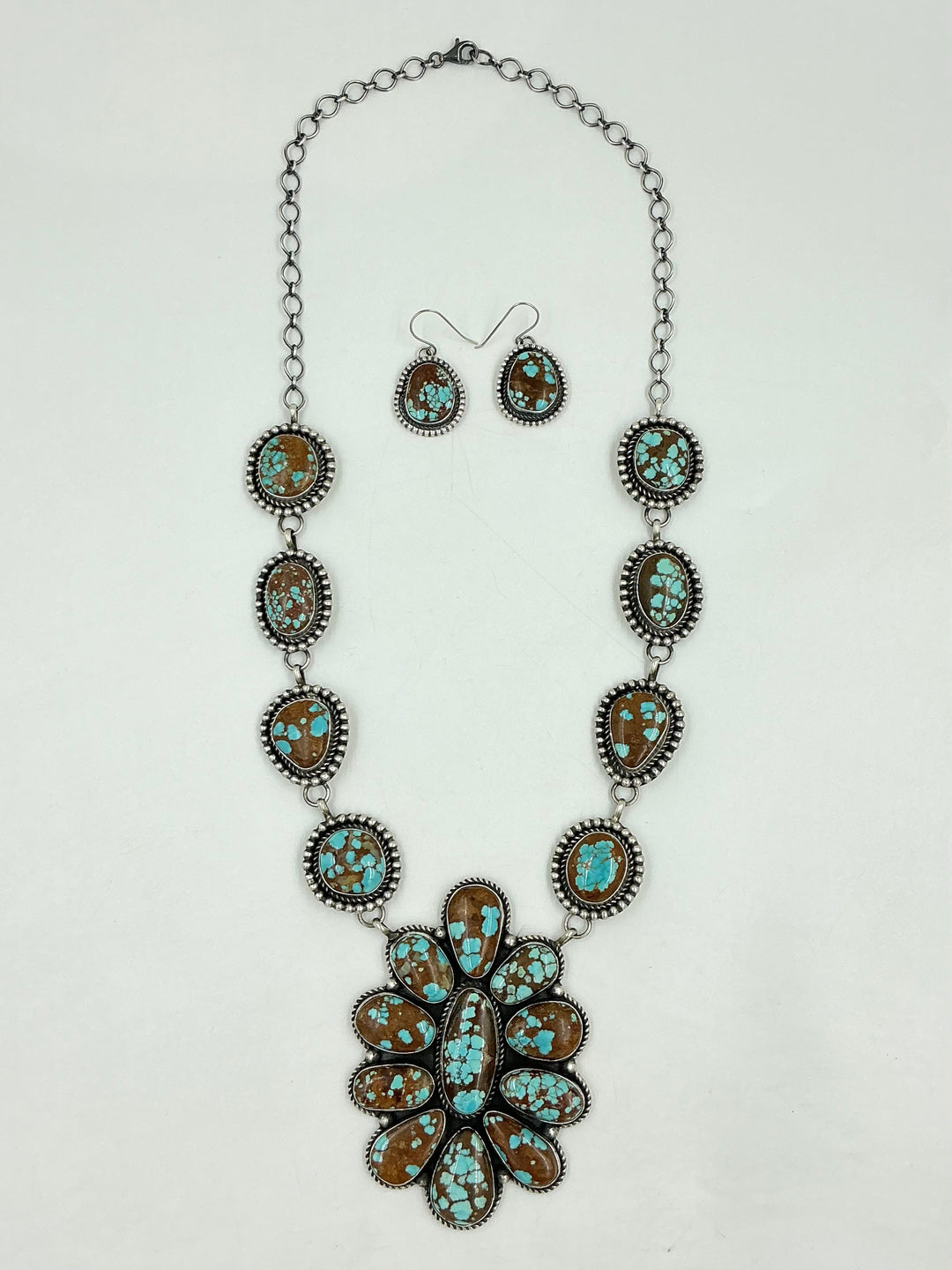 Turquoise Necklace with brown and blue stones in a center cluster of many in a flower and side stones set in sterling silver on a chain with a white background and earrings. 