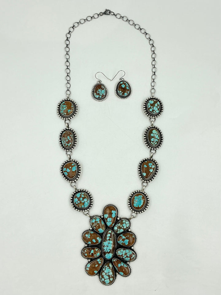 Turquoise Necklace with brown and blue stones in a center cluster of many in a flower and side stones set in sterling silver on a chain with a white background and earrings. 