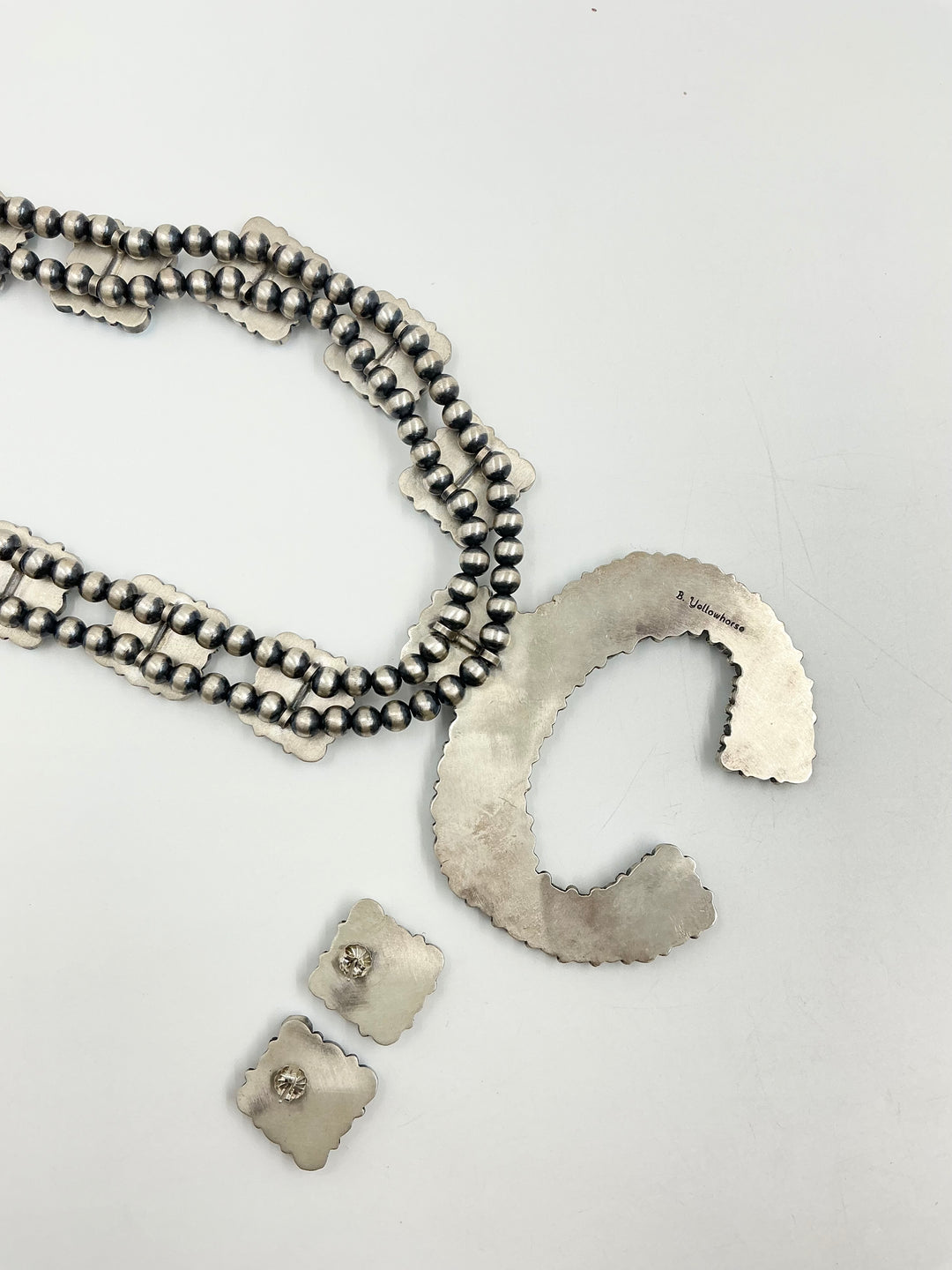 Silver back of Golden Hills turquoise necklace and earrings set with light blue and lavender colored stones with small cluster square formations showing stamped silver on a white background. 