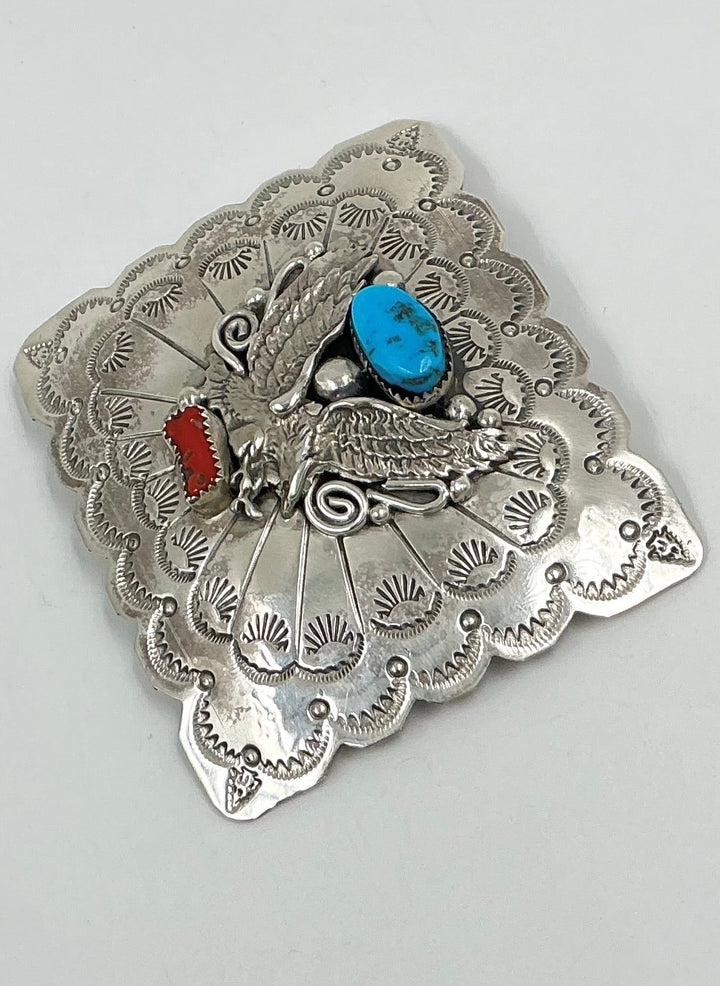 Silver brooch with intricate designs and colored stones on a light gray background