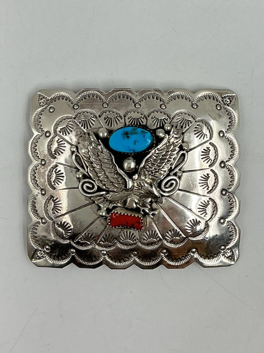 Silver belt buckle with eagle design and turquoise stone on a gray background
