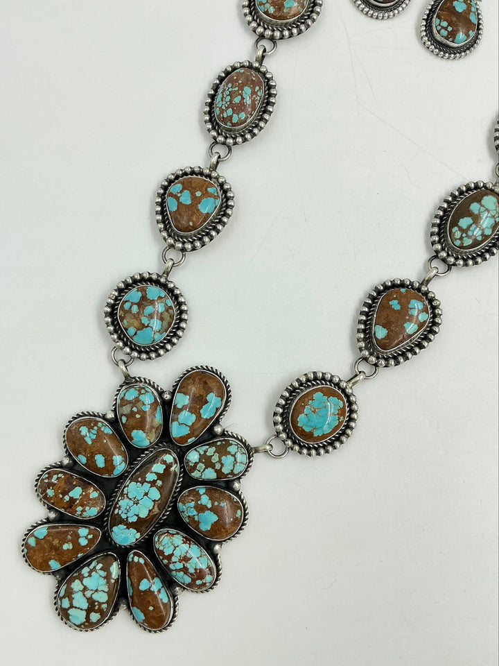 Turquoise Necklace with brown and blue stones in a center cluster of many in a flower and side stones set in sterling silver on a chain with a white background and earrings. 