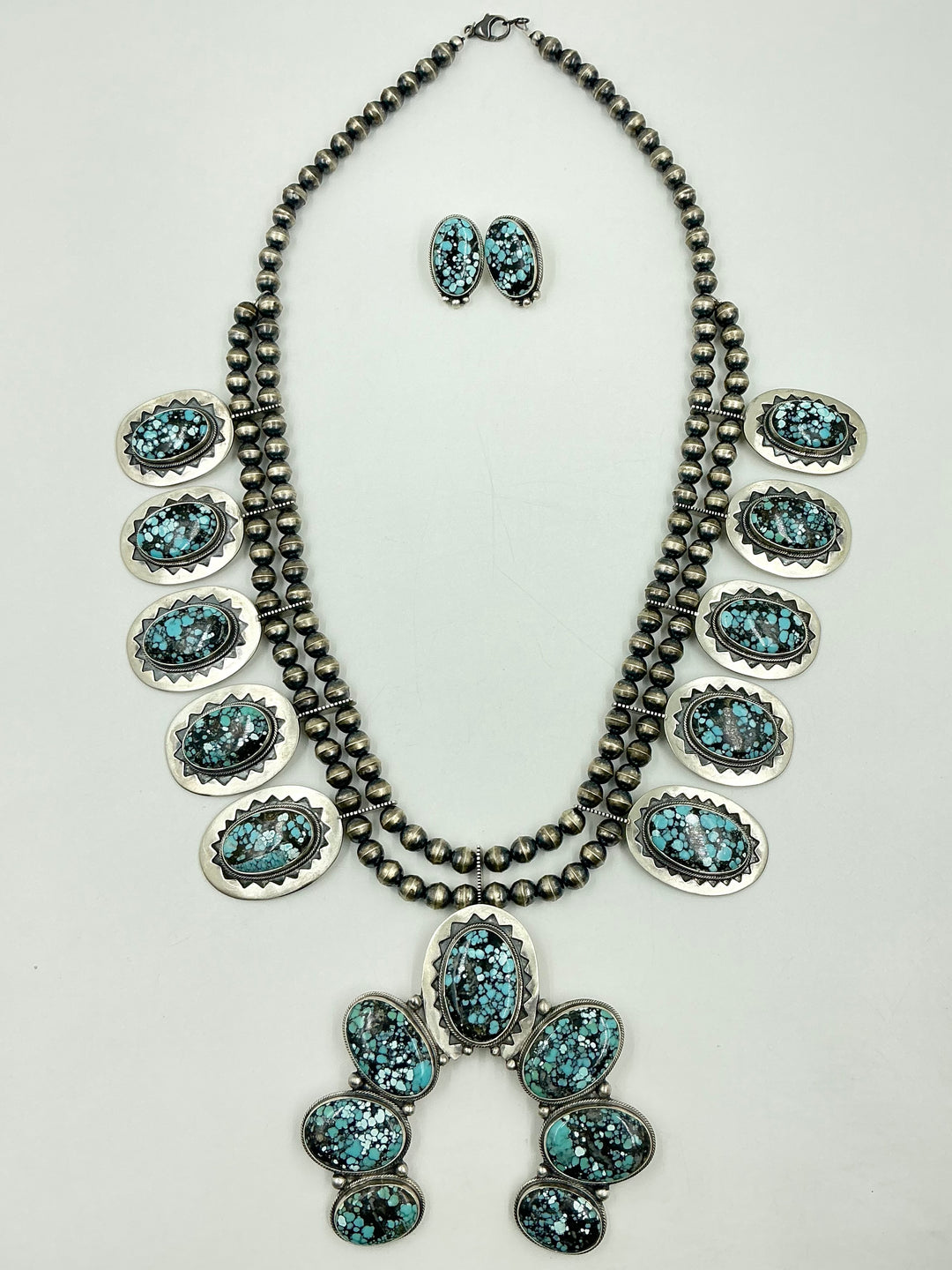 Jewelry set with necklace, earrings, and Naja pendant on a light gray background