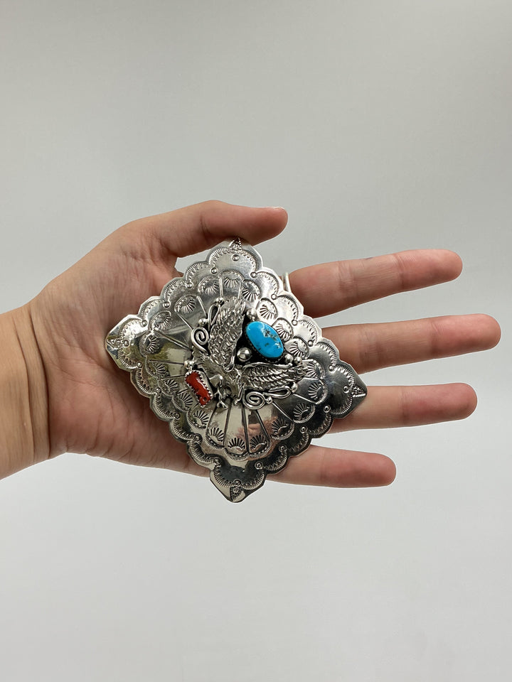 Hand wearing a decorative silver bracelet with colorful stones on a plain background