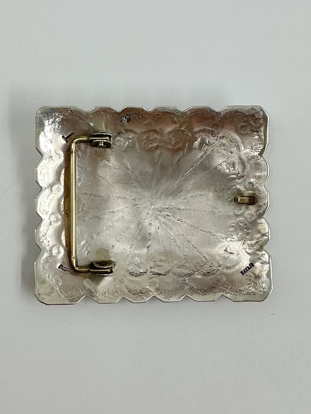 Silver brooch with textured surface on a light gray background