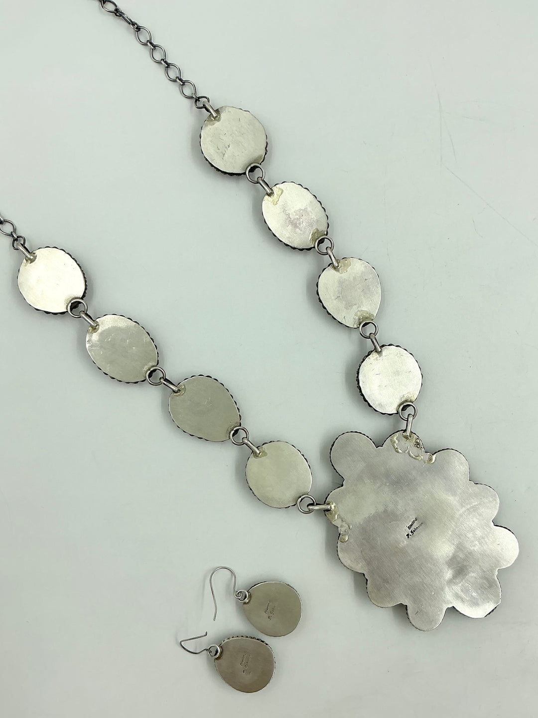 Silver back of turquoise Necklace on sterling silver on a chain showing stamped silver on a white background and earrings. 