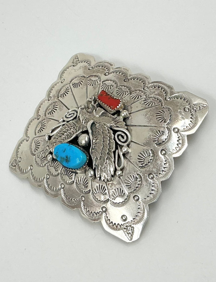 Silver belt buckle with turquoise and red stones on a light gray background