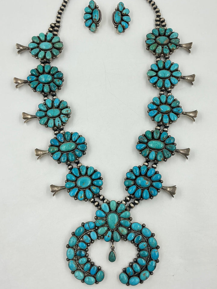 Kingman turquoise squash blossom necklace and earrings set with teal colored stones on a white background