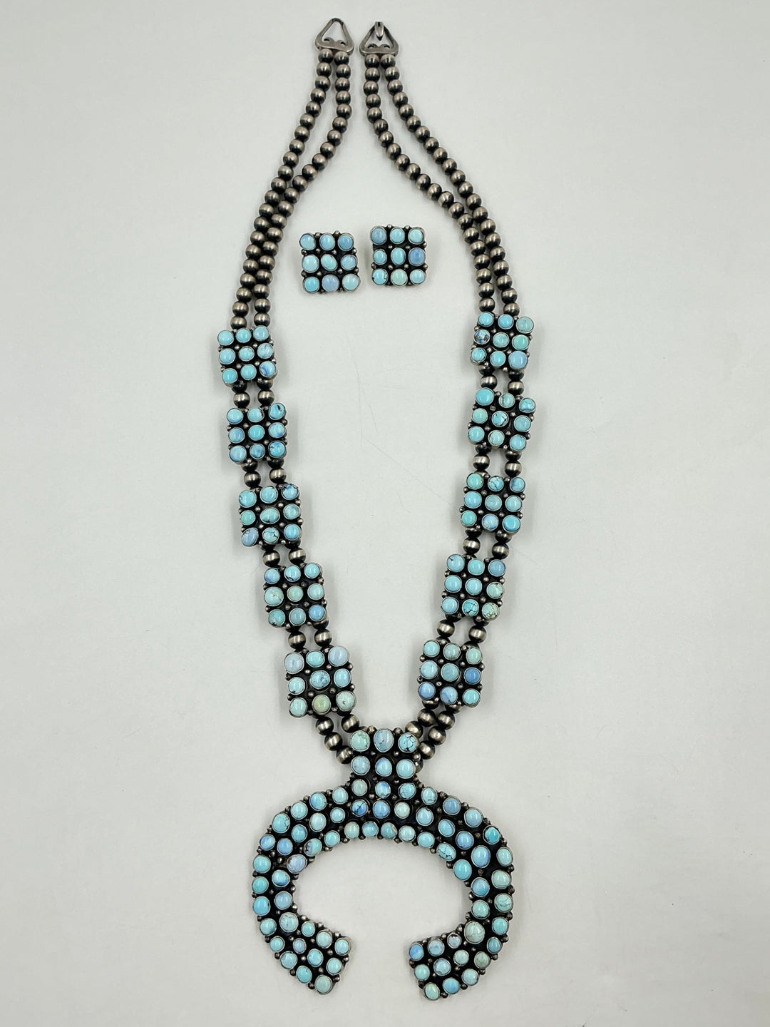 Golden Hills turquoise necklace and earrings set with light blue and lavender colored stones set in sterling silver with small cluster square formations on a white background. 