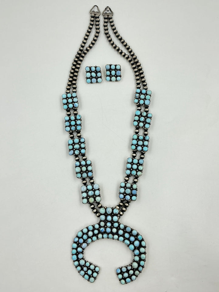 Golden Hills turquoise necklace and earrings set with light blue and lavender colored stones set in sterling silver with small cluster square formations on a white background. 