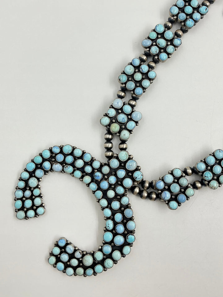Golden Hills turquoise necklace and earrings set with light blue and lavender colored stones set in sterling silver with small cluster square formations on a white background. 