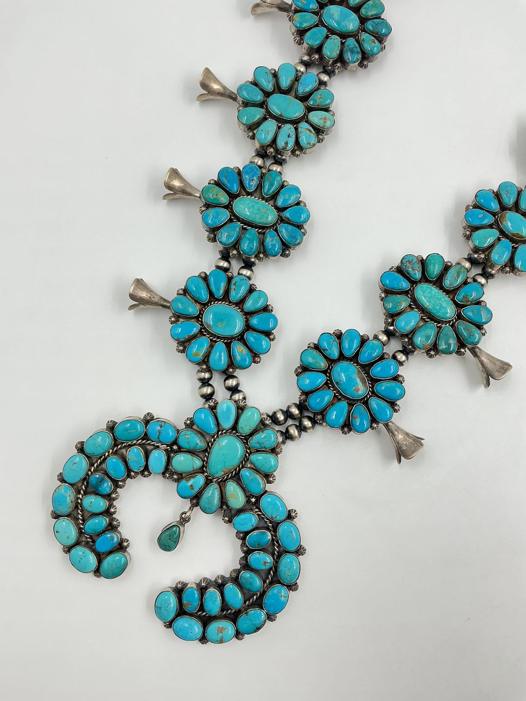 Kingman turquoise squash blossom necklace and earrings set with teal colored stones on a white background