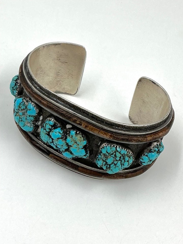 Silver cuff bracelet with turquoise stones on a white background
