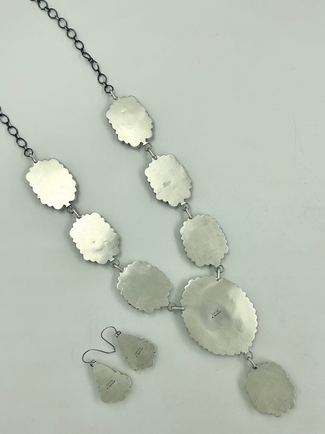 Silver back of necklace and earrings on a light gray background