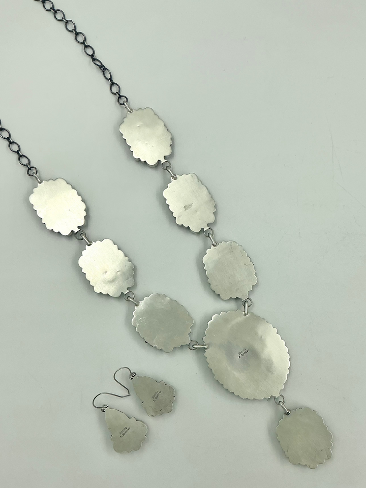 Silver back of necklace and earrings on a light gray background