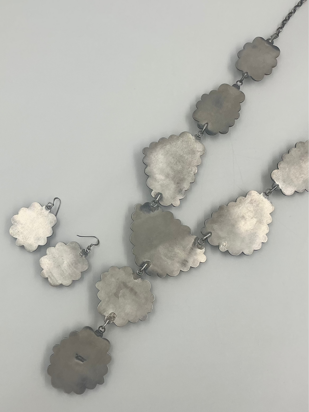 Silver back of necklace and earrings on a light gray background
