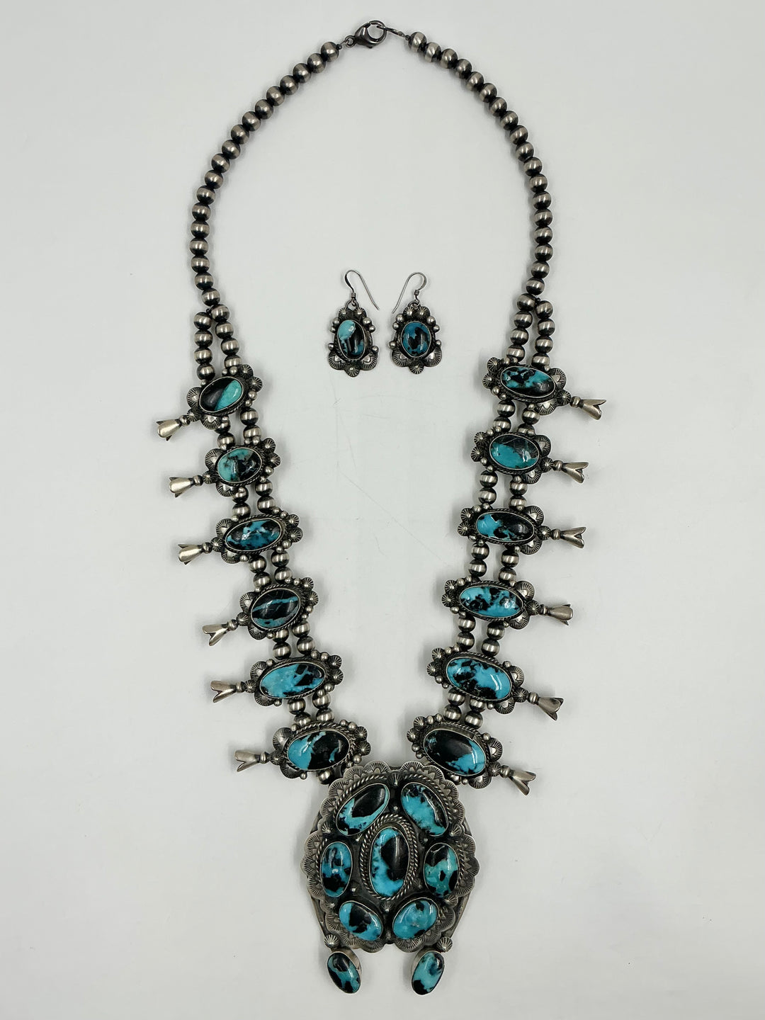 Squash blossom necklace and earrings set with blue stones on a white background