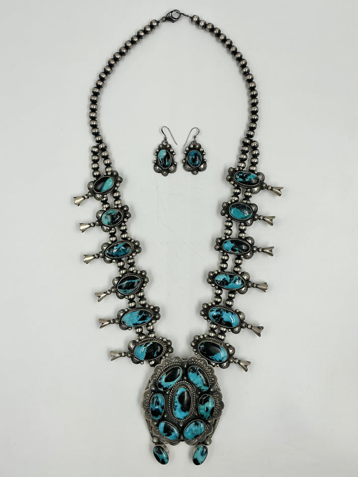 Squash blossom necklace and earrings set with blue stones on a white background
