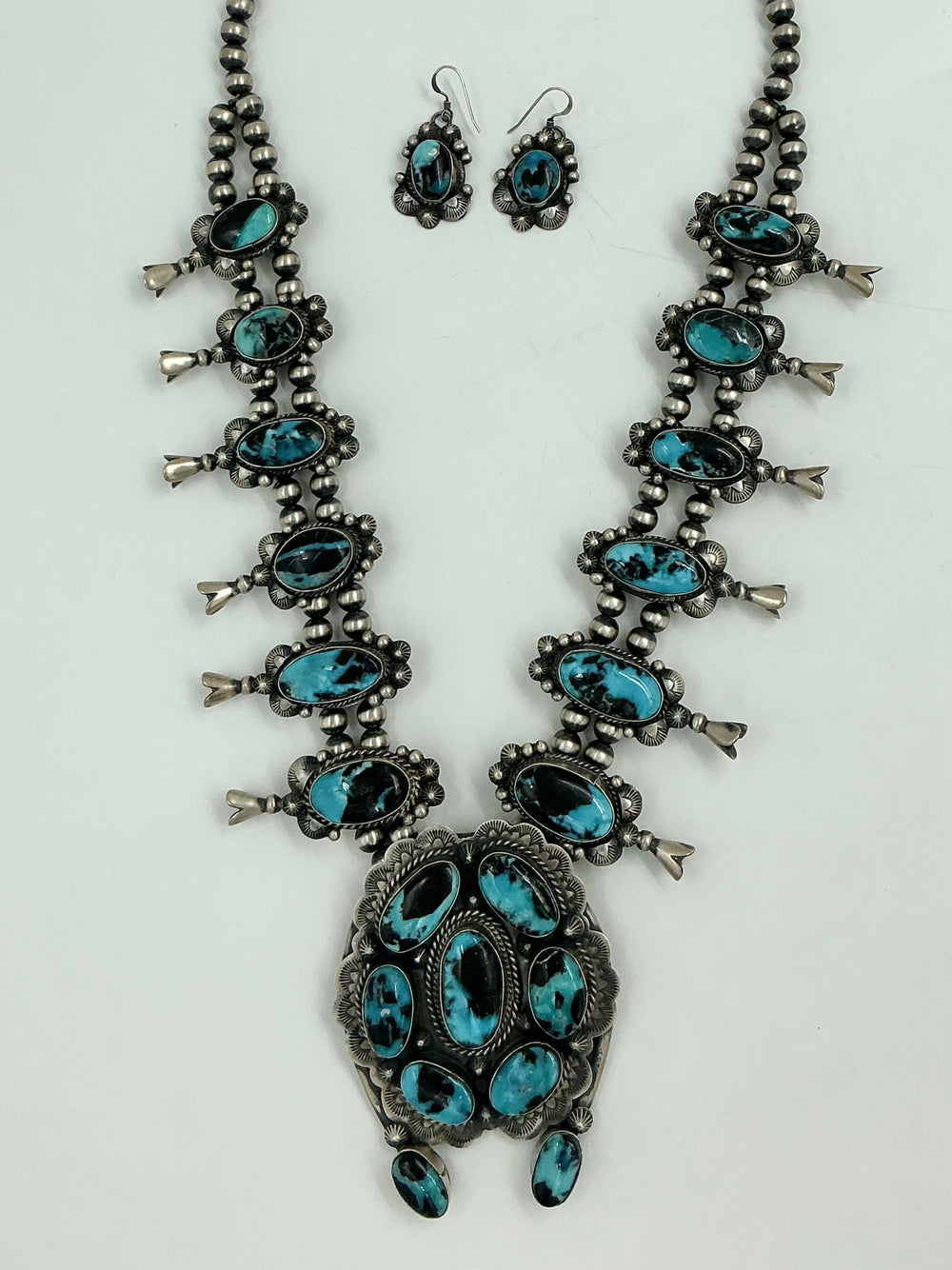 Squash blossom necklace and earrings set with blue stones on a white background