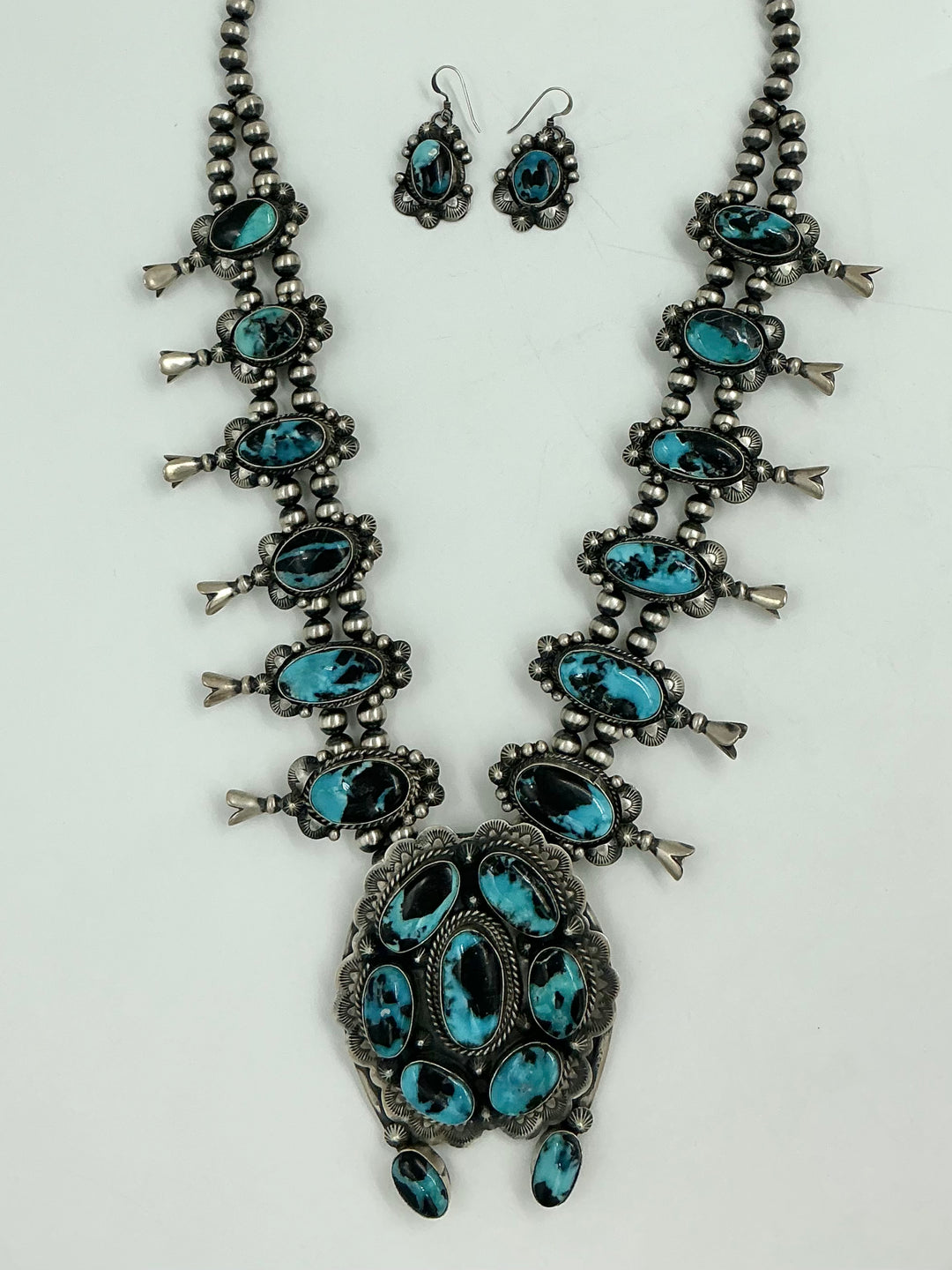 Squash blossom necklace and earrings set with blue stones on a white background