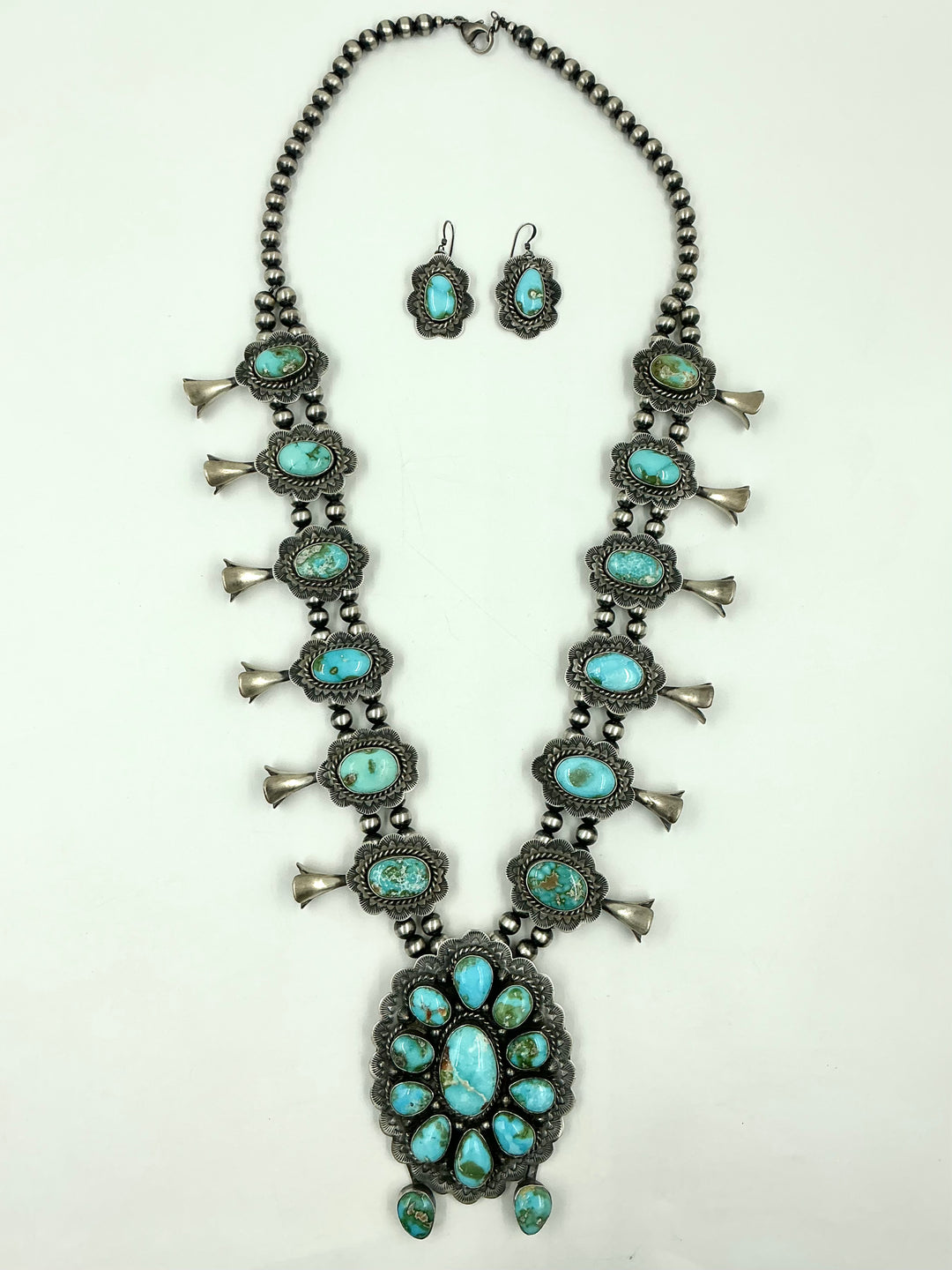 Squash blossom necklace and earrings set with blue/green stones on a white background