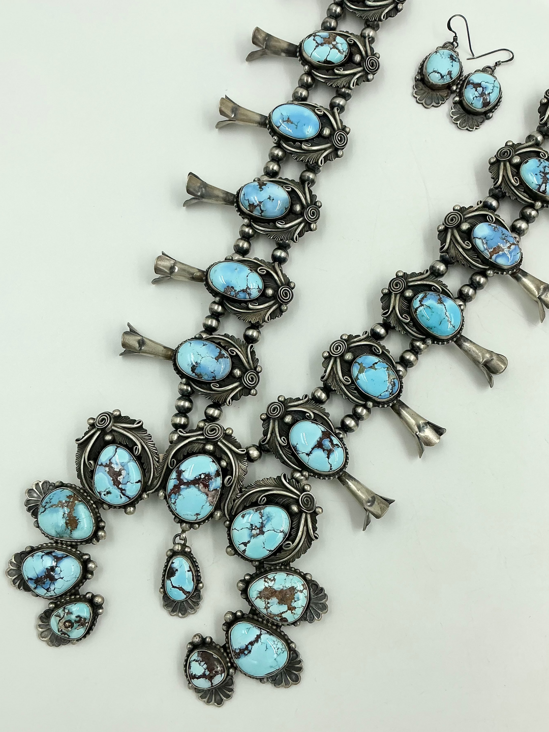 Turquoise stone necklace on sterling silver with leaf accents and earrings on a light gray background