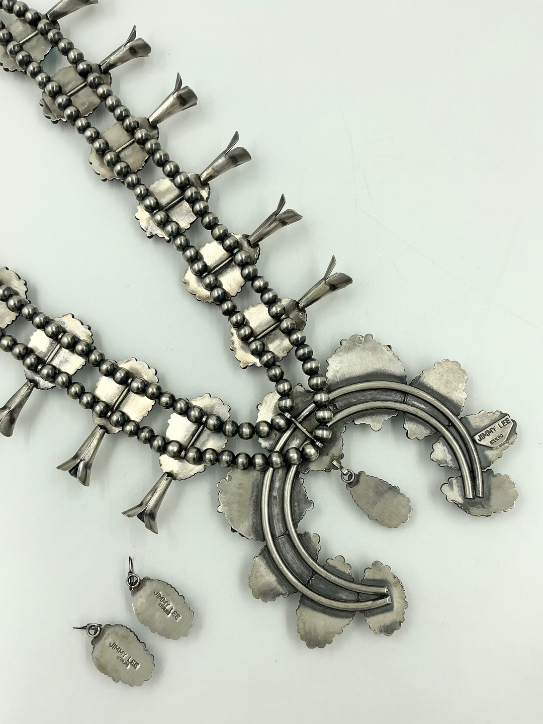 Silver back of turquoise stone necklace on sterling silver with leaf accents and earrings on a light gray background