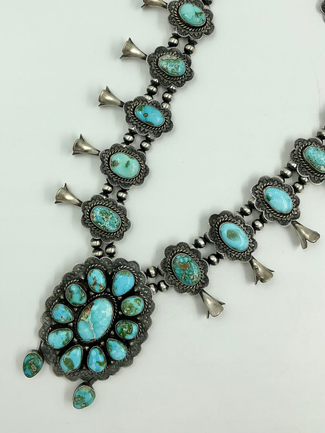 Squash blossom necklace and earrings set with blue/green stones on a white background