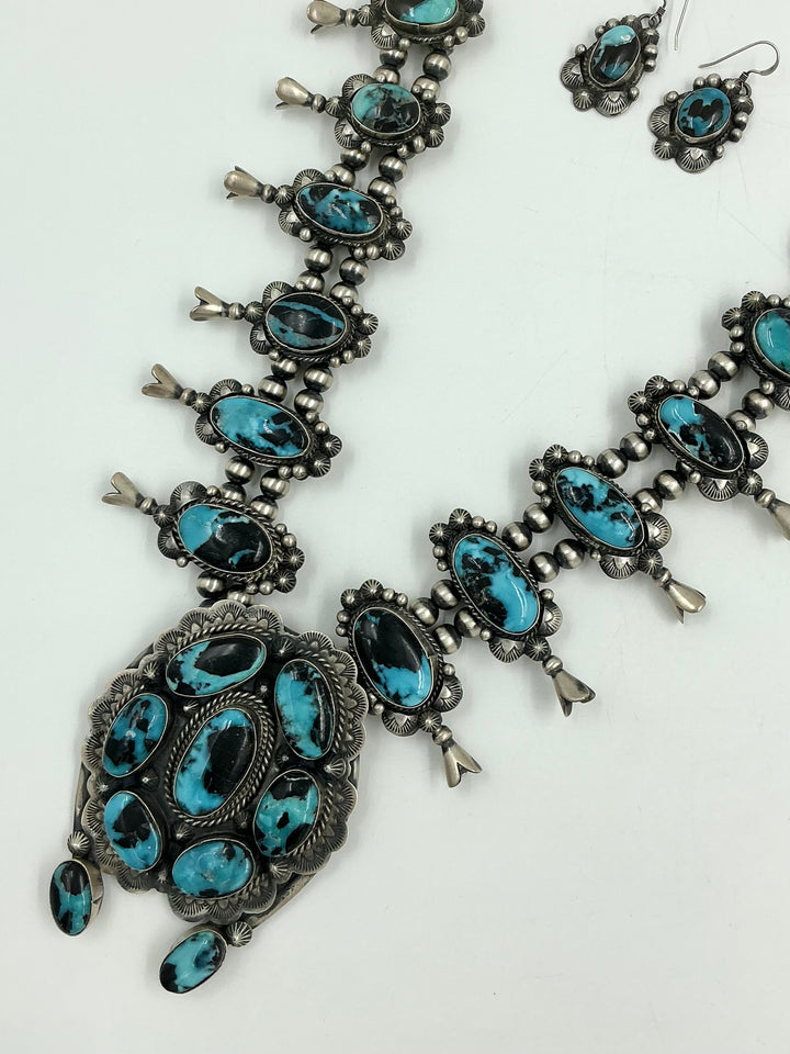 Squash blossom necklace and earrings set with blue stones on a white background