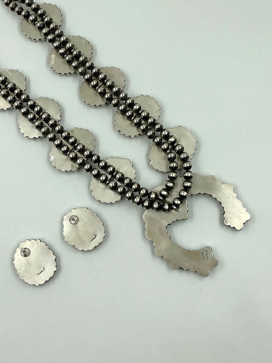 Silver back of turquoise stone necklace and earrings on a white background