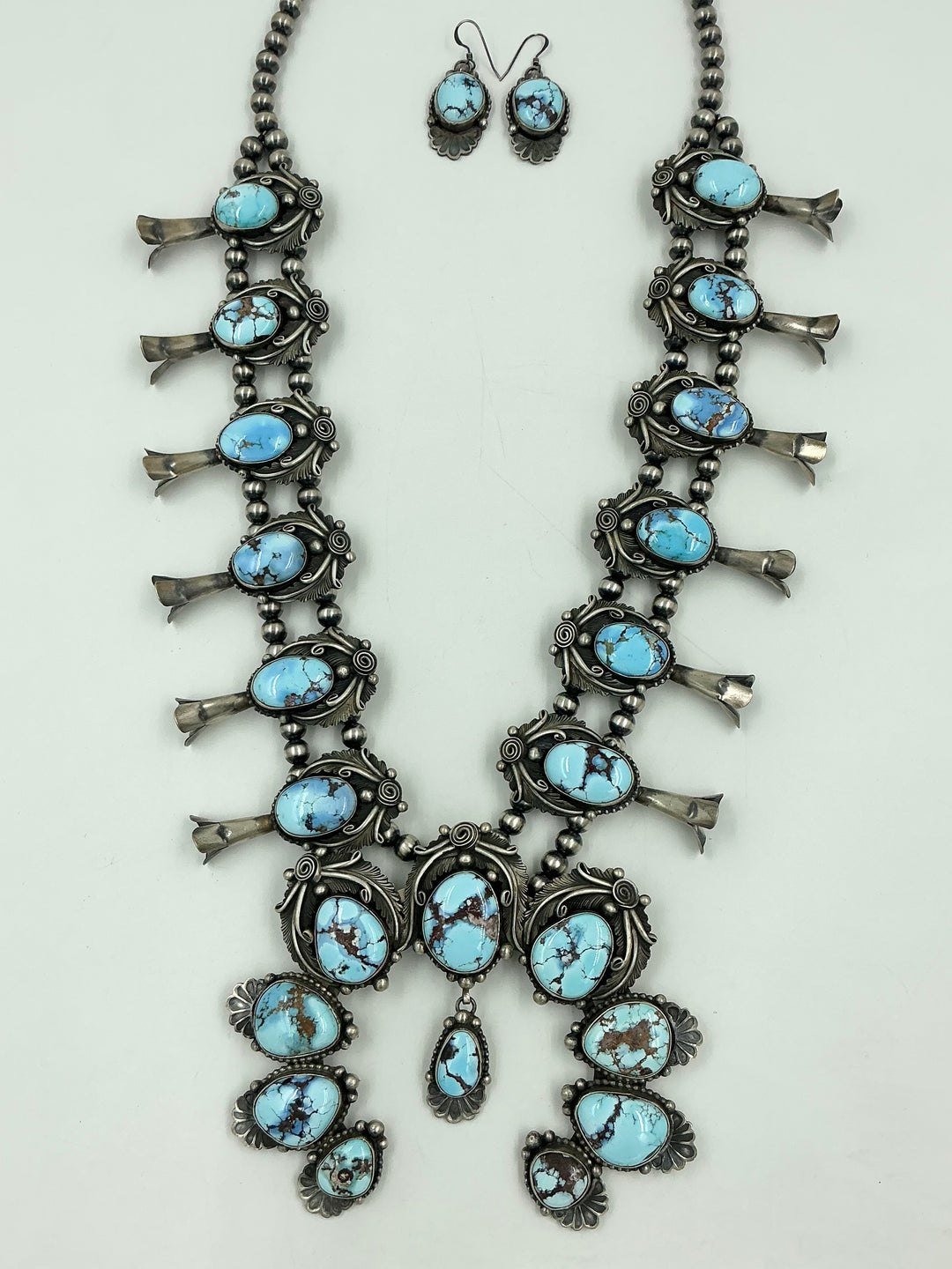 Turquoise stone necklace on sterling silver with leaf accents and earrings on a light gray background