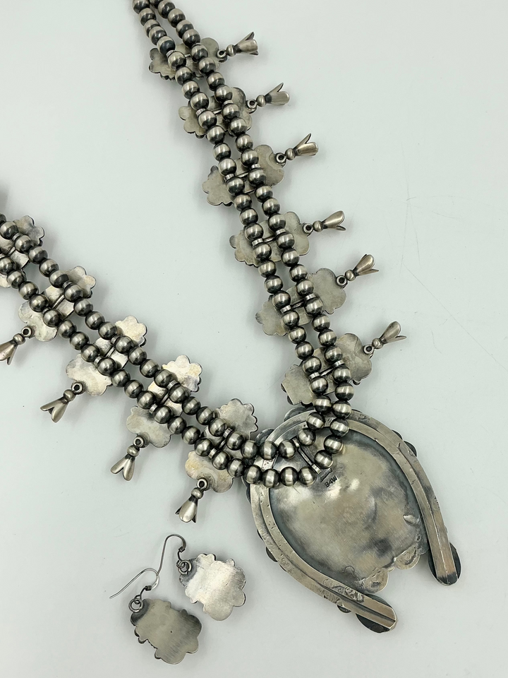 Silver back of squash blossom necklace and earrings set with blue stones on a white background