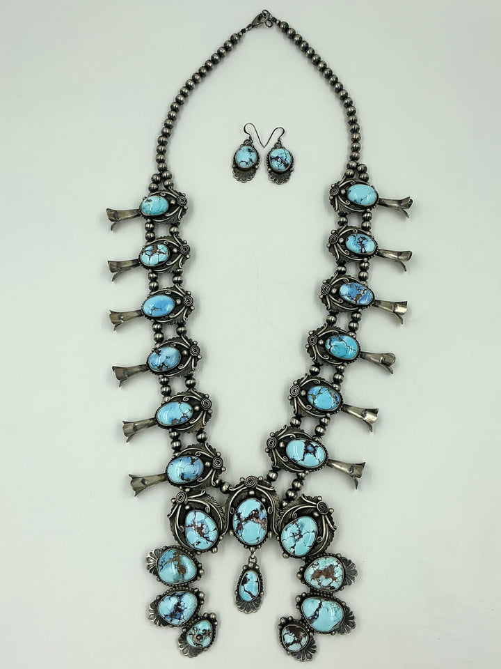 Turquoise stone necklace on sterling silver with leaf accents and earrings on a light gray background